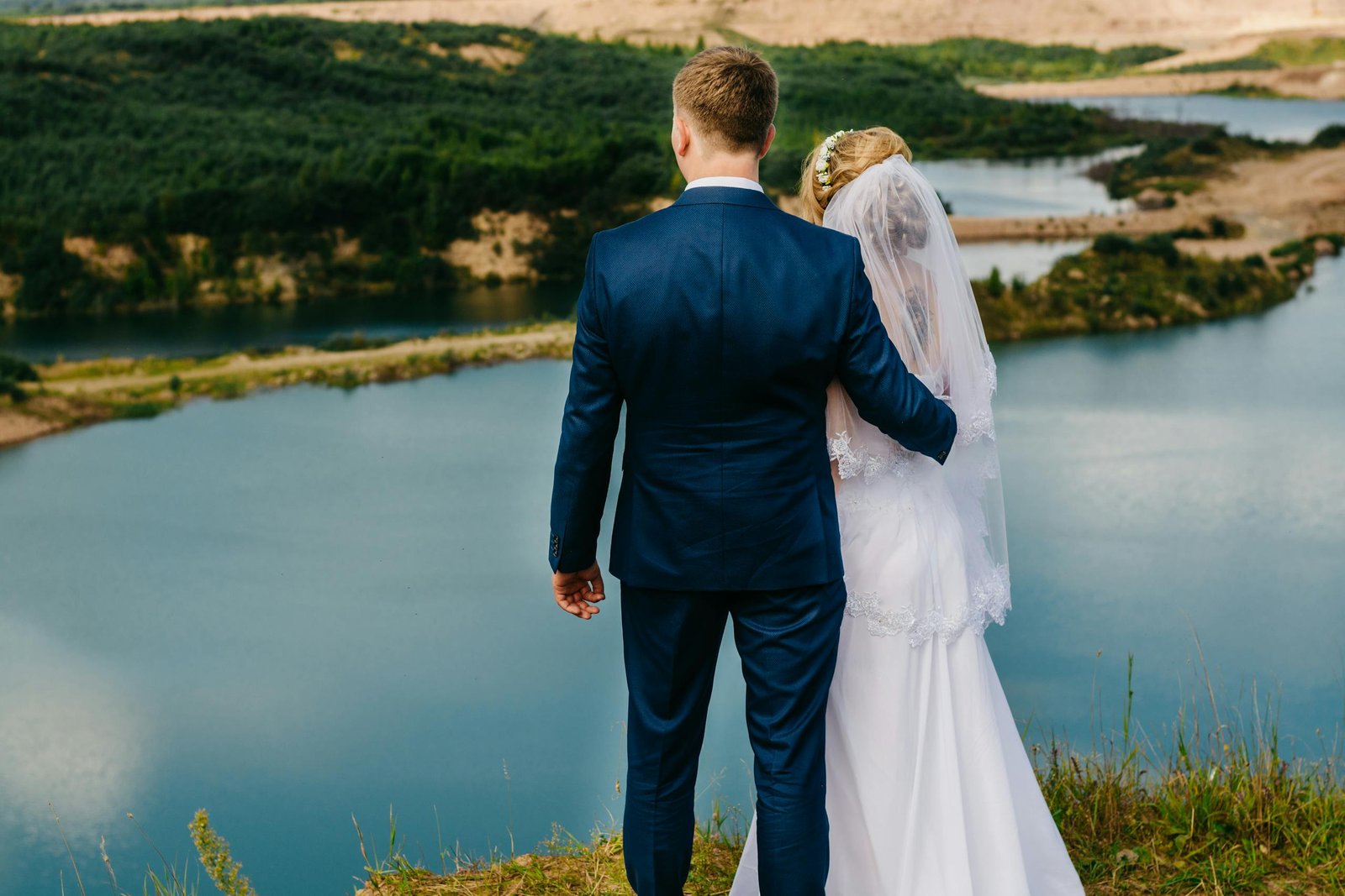 Bride and groom embracing on a cliff with stunning lake view, perfect for a romantic wedding moment.